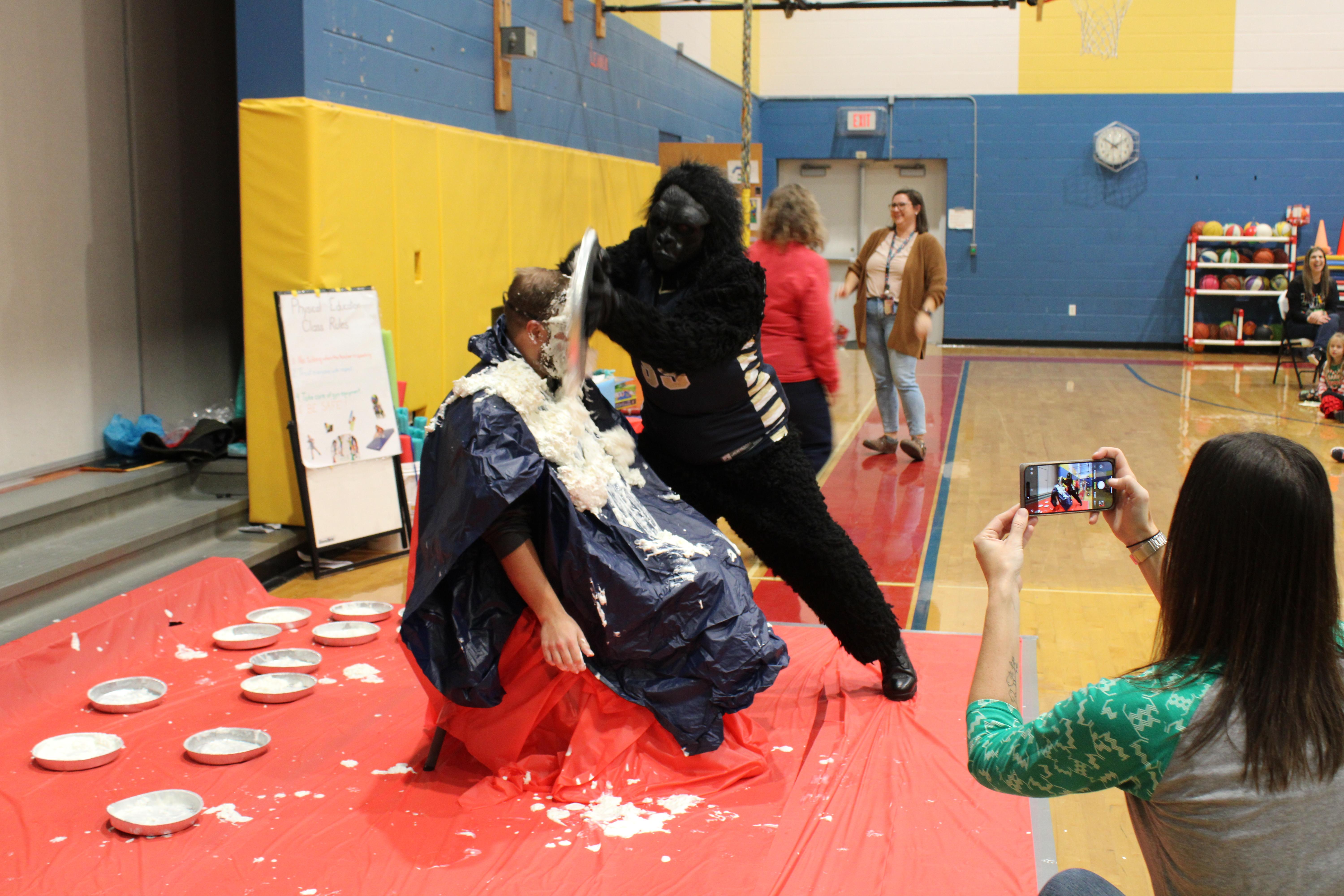 pic of a gorilla putting a pie in the face of a seated man